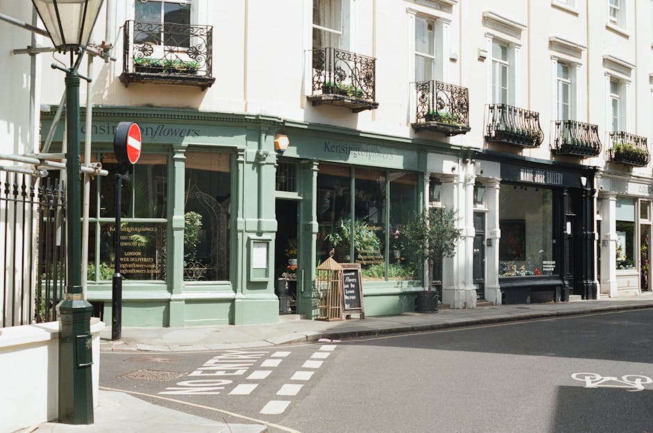 A row of white terraced houses in West Kensington featuring black wrought iron fences along the pavement. The image shows clean, well-maintained ceramic tiles on the walkway, with some patches of moss